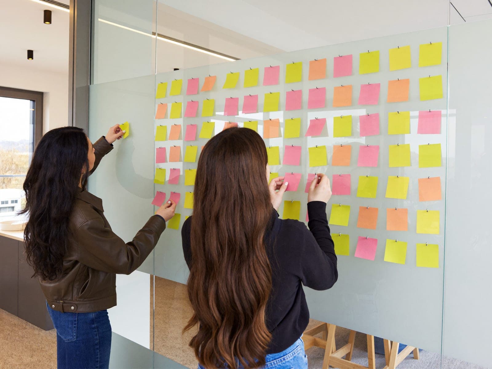 Two colleagues arranging notes on a glass wall to map a user journey