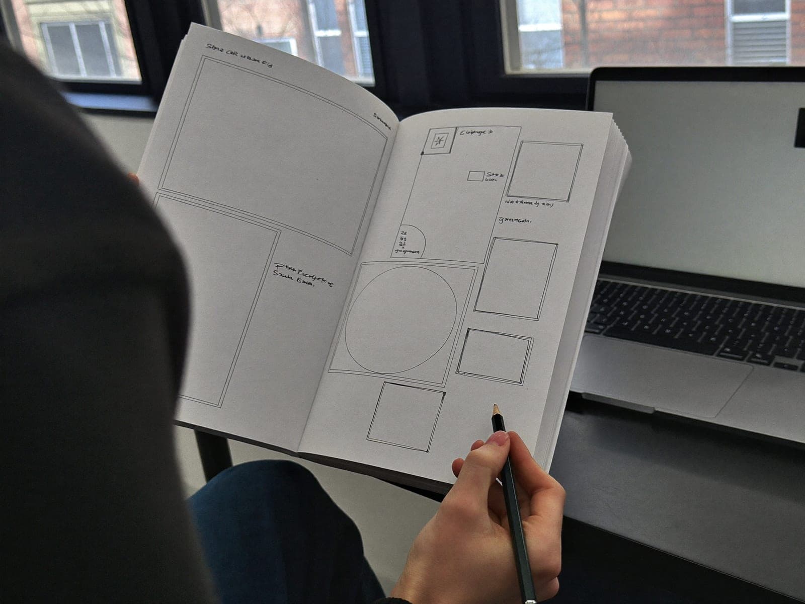 Designer sketching page layouts in a notebook beside a laptop